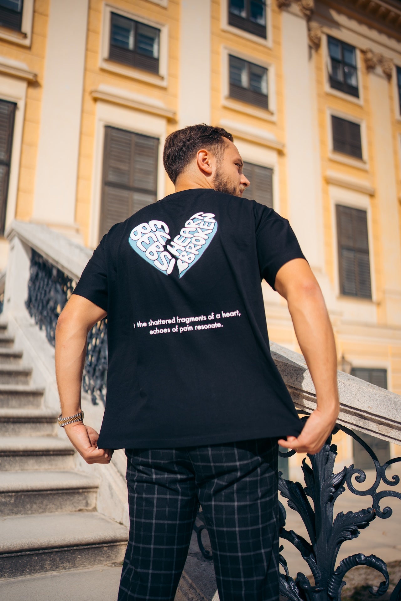 Man wearing a black t-shirt with a blue heart design on the back, standing outdoors.