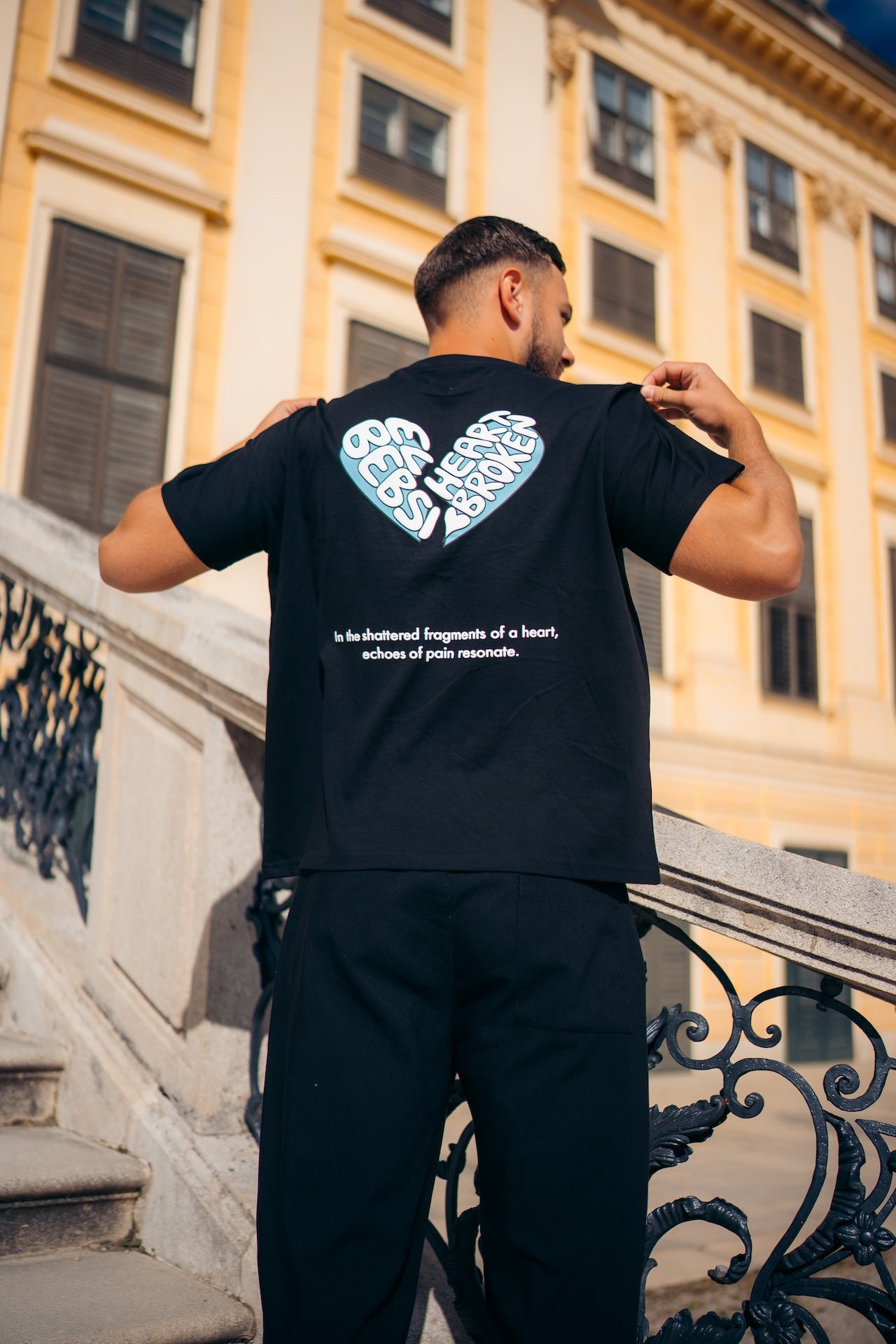 Man wearing a black t-shirt with a heart design on the back, standing in front of a building.